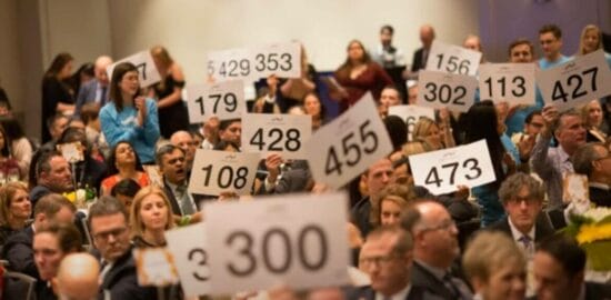 Tax liens Masachusetts auction - Crowd of bidders holding up numbered paddles at a live auction event.